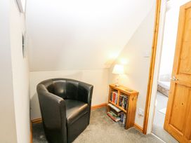 A small corner with a black armchair a wooden bookshelf with books and a lamp in a room at Lillies Pad Methwold near Feltwell