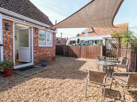 An outdoor patio area with gravel ground shading sail two glass tables and wicker chairs at Lillies Pad in Methwold near Feltwell