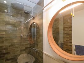 A bathroom with a shower and a round mirror at The Poop Deck in Coverack
