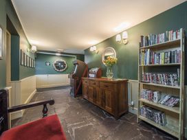 A hallway with green walls stone floor a wooden cabinet with flowers an arcade machine and a bookshelf at The Boars Head Pub in Bishops Castle