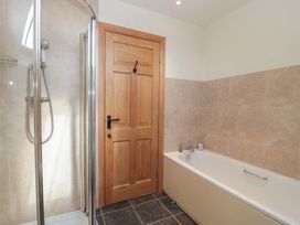 A bathroom with a shower, bathtub and wooden door at Bramble Cottage in Somerton