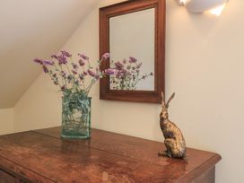 A wooden furniture with flowers in a vase and a rabbit statue at Bramble Cottage Babcary near Lydford-On-Fosse