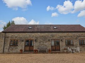 An exterior view of a stone house with a bench and flower pots at Badger Cottage in Lydford-On-Fosse