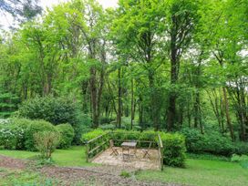An outdoor patio with a table and four chairs surrounded by trees and bushes at October Cottage in Chalford Gloucestershire