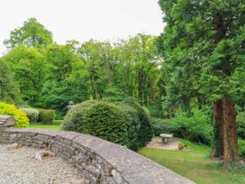 A garden with a stone wall gravel patio bushes trees and a small seating area at October Cottage in Chalford Gloucestershire