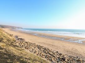 A sandy beach with scattered rocks and gentle waves under a clear sky at Lowena in Tywardreath