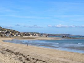 A sandy beach with people walking near the shoreline and a coastal village in the background at Lowena in Tywardreath