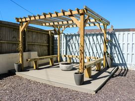 A pergola with benches and a fire pit in a garden at Rhiwlas Rhosneigr