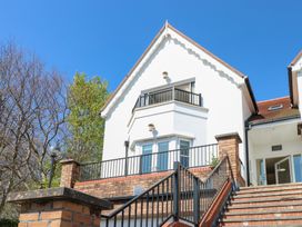 A white house with a red roof and black railings next to a staircase and trees at Cambrie in Tenby