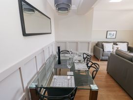 A dining area with a glass table set with placemats and glasses next to a living room with grey sofas and pillows at Cambrie in Tenby
