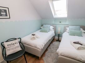A bedroom with two single beds a black chair with a cushion a small round table with a lamp and a skylight window at Cambrie in Tenby