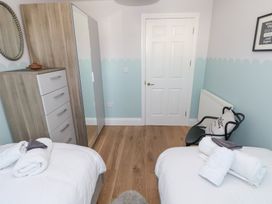 A bedroom with two single beds with white linens a wooden dresser with a mirror a black chair a door and light blue and white walls at Cambrie in Tenby