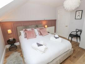 A bedroom with a double bed white bedding pink cushions bedside tables lamps a black chair and a door at Cambrie in Tenby