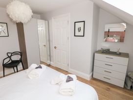 A bedroom with a bed, white towels, a black chair, a wardrobe with a mirrored door, a white door, framed pictures, a chest of drawers with a mirror, and wooden flooring at Cambrie in Tenby