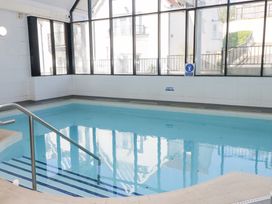 An indoor swimming pool with stairs and metal railing surrounded by large windows at Cambrie in Tenby
