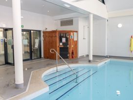 An indoor swimming pool with metal handrail steps a wooden sauna a shower a fire extinguisher and glass doors at Cambrie in Tenby