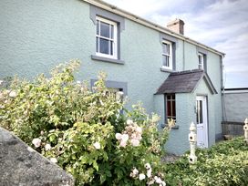 Exterior view of a pale blue textured house with white framed windows and a small porch surrounded by flowering bushes at The Farmhouse in Newport Pembrokeshire