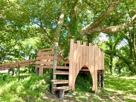 A wooden play structure with stairs and a slide built around a tree in a forest clearing at The Farmhouse in Newport Pembrokeshire