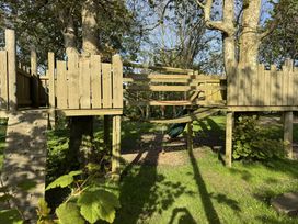 A wooden play structure with a climbing wall a bridge and a slide in a grassy outdoor area at The Farmhouse in Newport Pembrokeshire