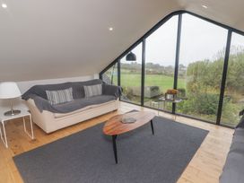 A living room with a sofa a wooden coffee table a floor lamp and large windows overlooking a grassy field at The Willows in Newport Pembrokeshire