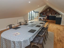 A dining area with a long table covered with a patterned cloth and metal chairs next to a kitchen with a brick backsplash at The Willows in Newport Pembrokeshire