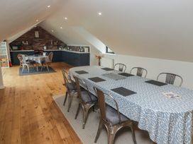 A dining area with a long table covered with a blue and white tablecloth and metal chairs and a kitchen with a smaller round table in an attic space at The Willows in Newport Pembrokeshire