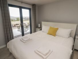 A bedroom with a bed with white bedding and a yellow cushion and two folded towels on the bed by a glass door with curtains at The Willows in Newport Pembrokeshire