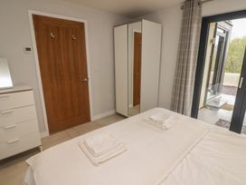 A bedroom with a bed with folded towels on it a white dresser a wooden door a white wardrobe with a mirror and sliding glass doors with curtains at The Willows in Newport Pembrokeshire