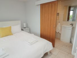 A bedroom with a white bed with folded towels and a yellow pillow next to a wooden sliding door leading to a small bathroom with a sink at The Willows in Newport Pembrokeshire
