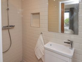 A bathroom shower area with white tiled walls a wall niche a towel on a hook a white sink with a faucet and a mirror reflecting a window at The Willows Newport Pembrokeshire