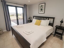 A bedroom with a black bed frame white bedding yellow pillow bedside tables with lamps and glass doors at The Willows in Newport Pembrokeshire