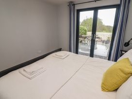 A bedroom with a bed towel sets and a yellow pillow next to glass doors with blue curtains at The Willows in Newport Pembrokeshire