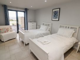 A bedroom with two single beds a white dresser and glass doors with blue curtains at The Willows in Newport Pembrokeshire