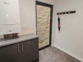 A utility room with a countertop cabinet boiler electric sockets umbrella on a wall hook and glass door showing stone wall outside at The Willows in Newport Pembrokeshire