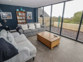 A living room with two sofas a wooden coffee table a bookshelf and large glass windows at The Willows in Newport Pembrokeshire