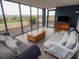 A living room with sofas a wooden coffee table a chest of drawers and large glass windows at The Willows in Newport Pembrokeshire