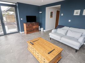 A living room with a wooden TV stand and coffee table a gray sofa and glass door at The Willows in Newport Pembrokeshire