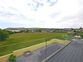 A balcony with a small table and chairs overlooking a green field and houses at The Willows in Newport Pembrokeshire