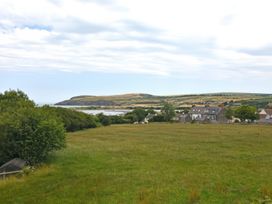A grassy field with trees and houses overlooking a body of water and hills in the distance at The Willows in Newport Pembrokeshire