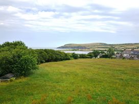A grassy field with trees on the left and houses on the right overlooking a body of water and hills at The Willows in Newport Pembrokeshire