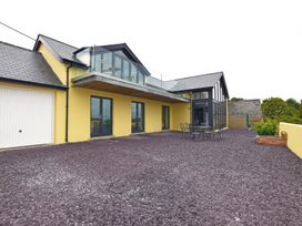 A yellow house with black-framed windows and glass balcony over a patio with outdoor table and chairs at The Willows in Newport Pembrokeshire