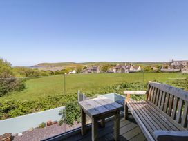 An outdoor area with a bench and table overlooking a field and houses at The Willows in Newport, Pembrokeshire