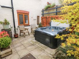 An outdoor patio with a hot tub two wooden chairs potted plants and a wooden fence at Mill Barn Denant in Haverfordwest Pembrokeshire