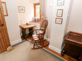 A corner of a room with a wooden rocking chair a small wooden table with a lamp books on a windowsill and framed pictures on the wall at Mill Barn Denant Haverfordwest Pembrokeshire