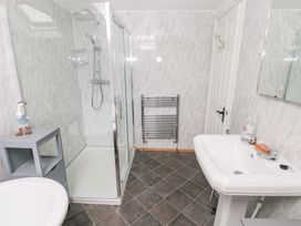 A bathroom with a glass shower enclosure a white sink a gray storage unit a towel rack and tiled floor at Mill Barn Denant in Haverfordwest Pembrokeshire