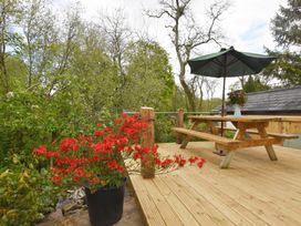 An outdoor wooden deck with a picnic table and green umbrella with red flowers in a pot at Mill Barn Denant in Haverfordwest Pembrokeshire
