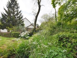 A garden with tall trees bushes and white flowers near a house with white walls at Mill Barn Denant in Haverfordwest Pembrokeshire