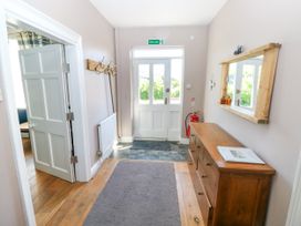 An entrance hallway with a wooden dresser and mirror on the right wall a coat rack on the left wall and a white door with a fire exit sign above at Newton West Farm Newton near Newgale