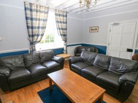 A living room with two black leather sofas a wooden coffee table checked curtains and a brown armchair at Newton West Farm Newton near Newgale