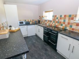 A kitchen with white cabinets black countertops a black stove dishwasher microwave and tiled backsplash at Newton West Farm in Newton near Newgale